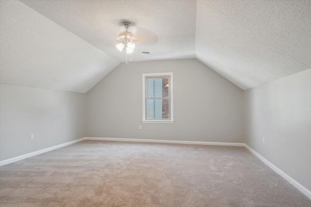 additional living space with lofted ceiling, light carpet, baseboards, and a textured ceiling