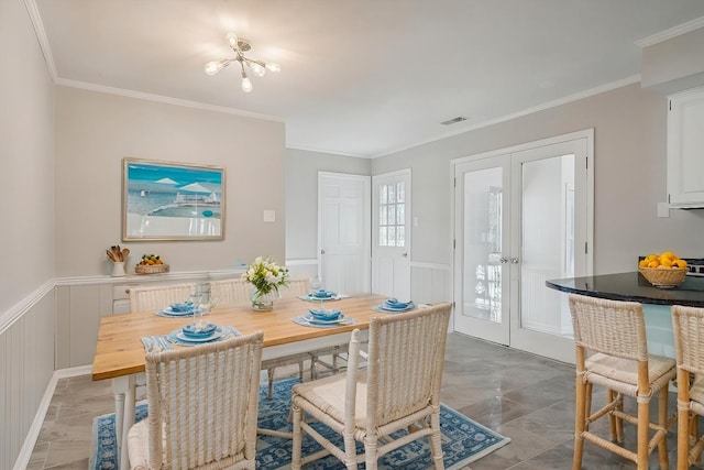 dining area with a wainscoted wall, visible vents, crown molding, and french doors