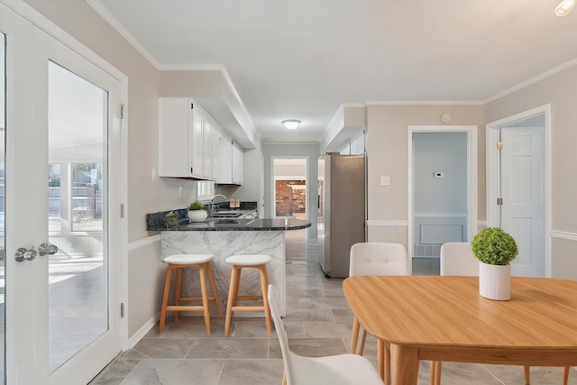 kitchen featuring a peninsula, a sink, white cabinetry, stainless steel fridge, and crown molding