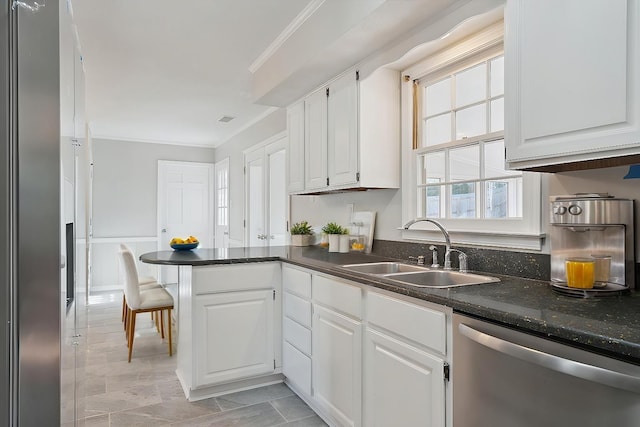 kitchen featuring white cabinets, dark countertops, ornamental molding, stainless steel dishwasher, and a sink