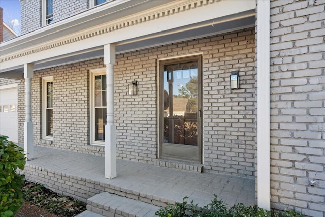 view of exterior entry featuring covered porch and brick siding