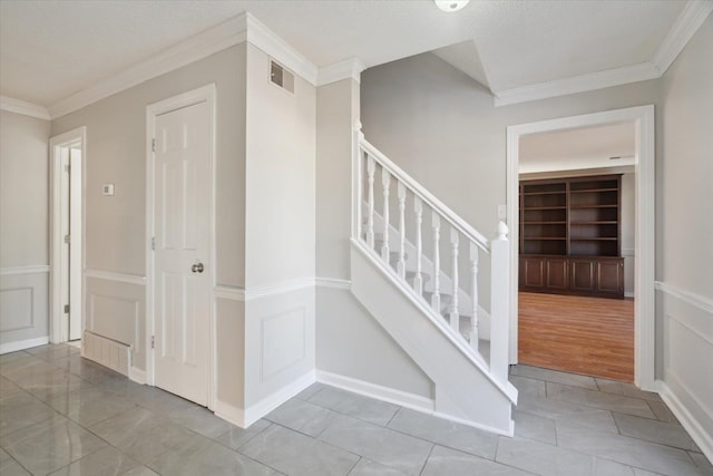 stairway featuring a decorative wall, wainscoting, built in shelves, and crown molding