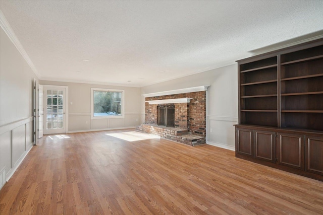 unfurnished living room with ornamental molding, a fireplace, a textured ceiling, and light wood finished floors