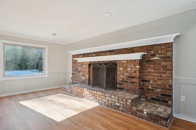 unfurnished living room featuring a fireplace, crown molding, a decorative wall, wainscoting, and wood finished floors