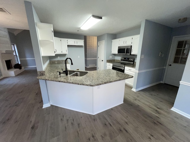 kitchen featuring dark stone countertops, kitchen peninsula, sink, appliances with stainless steel finishes, and white cabinets