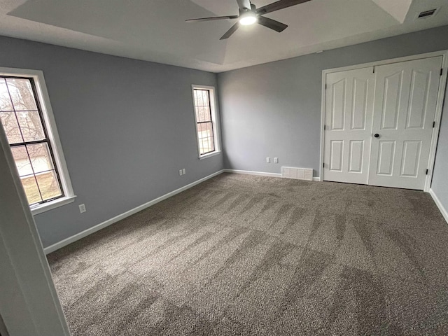 unfurnished bedroom with ceiling fan, a closet, a raised ceiling, and carpet flooring