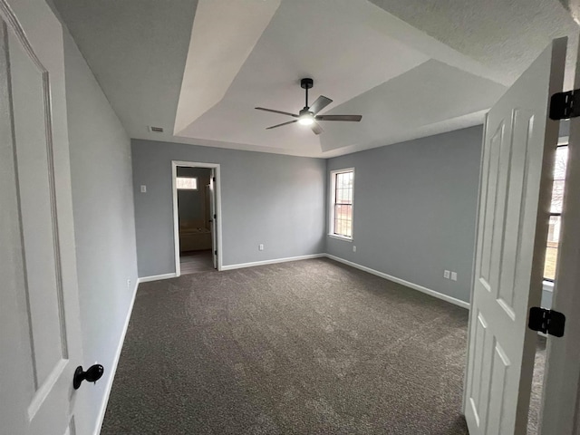 unfurnished bedroom featuring ceiling fan, a textured ceiling, a tray ceiling, and dark colored carpet