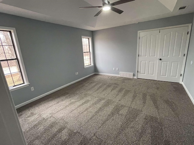 unfurnished bedroom with ceiling fan, multiple windows, a tray ceiling, and carpet flooring