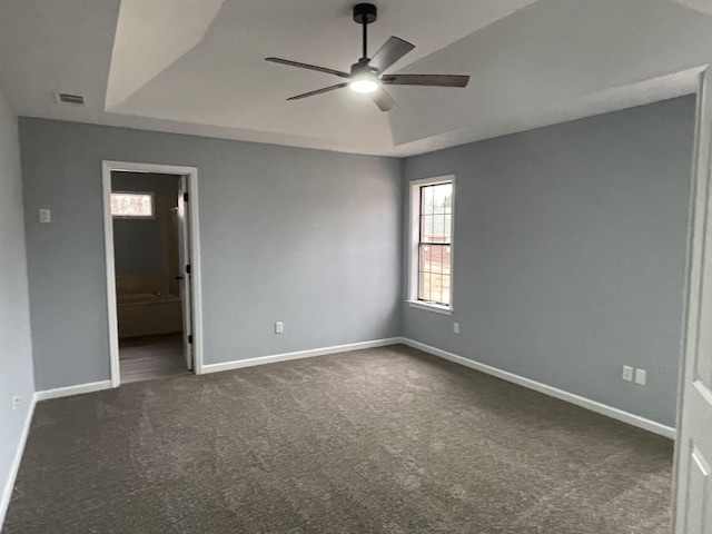 empty room with a raised ceiling, ceiling fan, and dark colored carpet