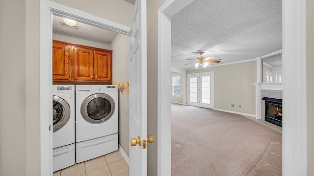 washroom with light tile patterned floors, ceiling fan, washer and dryer, cabinets, and a tile fireplace