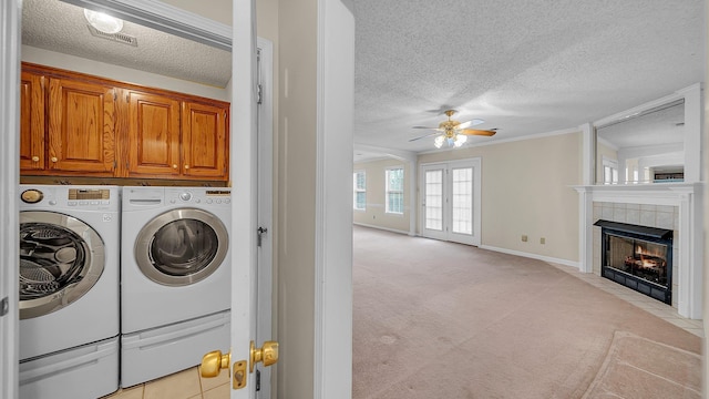 laundry area featuring ceiling fan, a fireplace, crown molding, washer and clothes dryer, and cabinets