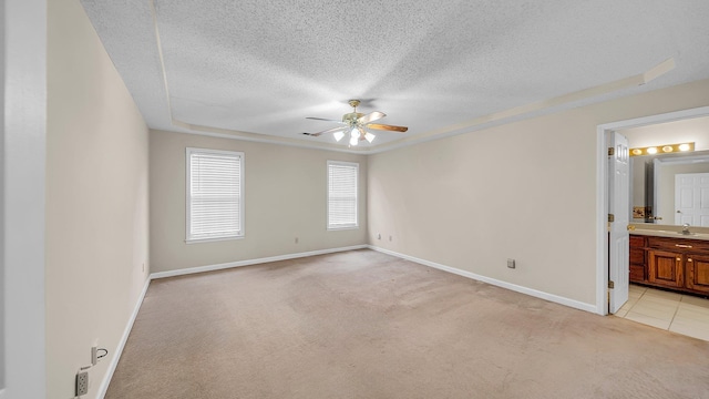 unfurnished bedroom with light carpet, ceiling fan, a textured ceiling, and ensuite bath