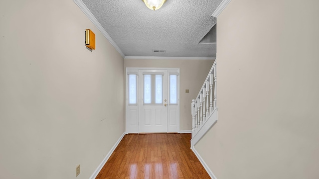 entryway with wood-type flooring, ornamental molding, and a textured ceiling