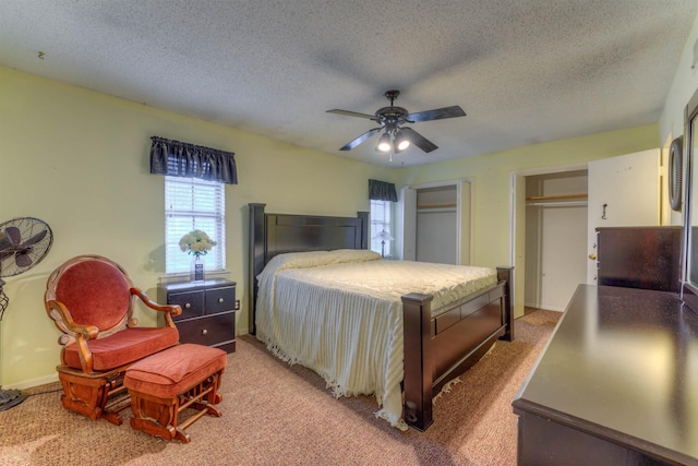 carpeted bedroom with a textured ceiling, ceiling fan, and two closets