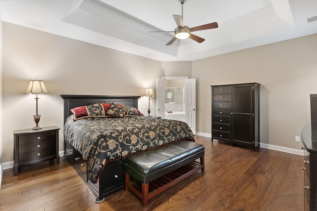 bedroom featuring ceiling fan, ensuite bath, dark hardwood / wood-style floors, and a raised ceiling