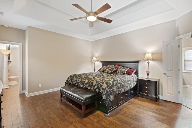 bedroom featuring a raised ceiling, ensuite bath, ceiling fan, and dark hardwood / wood-style flooring