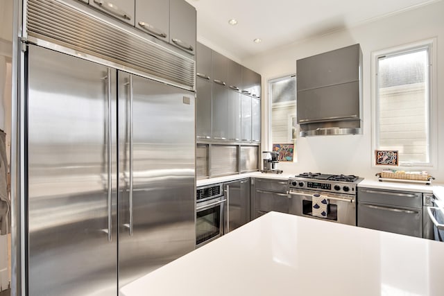 kitchen featuring crown molding, wall chimney range hood, gray cabinets, and stainless steel appliances