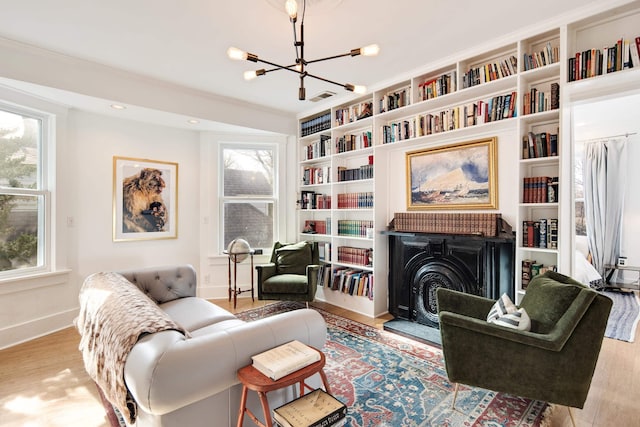 living room featuring built in shelves, ornamental molding, an inviting chandelier, and light wood-type flooring