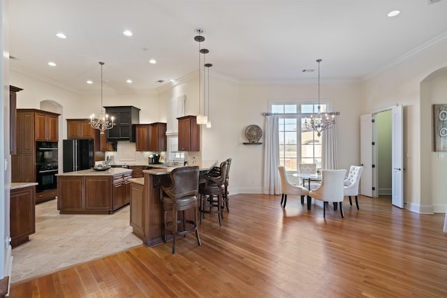 kitchen with black appliances, a kitchen island, a kitchen breakfast bar, hanging light fixtures, and a notable chandelier