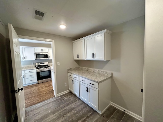 kitchen with light stone counters, appliances with stainless steel finishes, dark hardwood / wood-style floors, and white cabinets