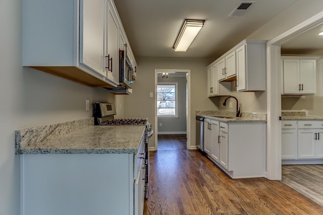 kitchen with wood-type flooring, sink, white cabinets, light stone counters, and stainless steel appliances