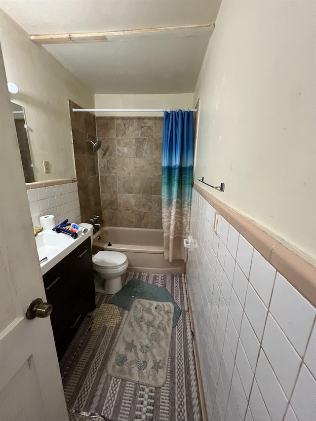 full bathroom with tile walls, toilet, vanity, and shower / tub combo with curtain