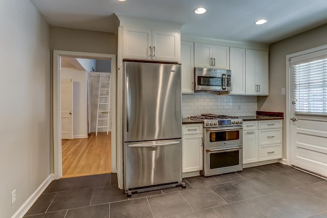 kitchen with dark tile patterned flooring, white cabinetry, stainless steel appliances, and tasteful backsplash