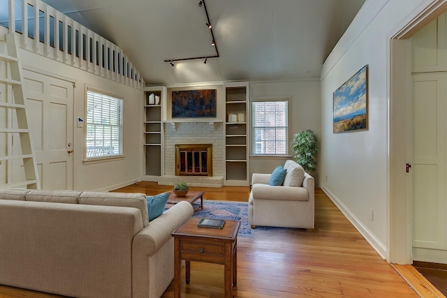 living room with light hardwood / wood-style flooring, vaulted ceiling, a fireplace, and rail lighting