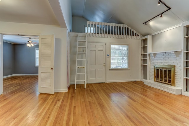 entryway featuring ceiling fan, vaulted ceiling, a brick fireplace, light hardwood / wood-style flooring, and rail lighting