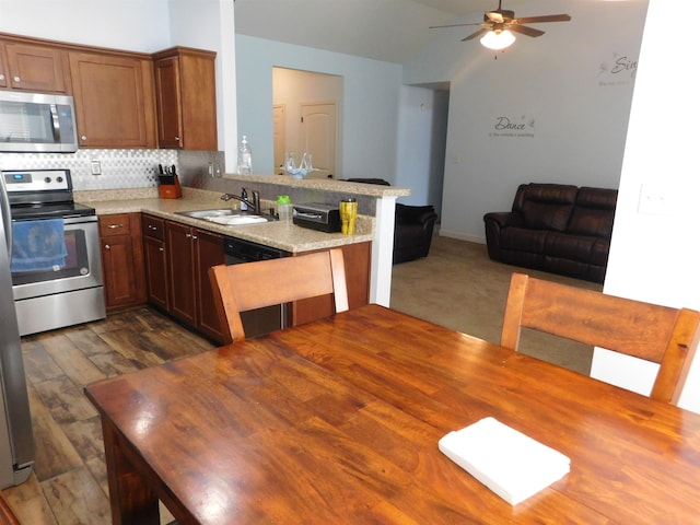 kitchen featuring a sink, backsplash, open floor plan, stainless steel appliances, and a peninsula