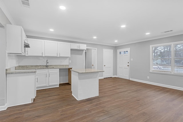 kitchen featuring a center island, sink, white cabinetry, ornamental molding, and light stone counters