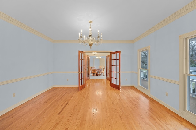 unfurnished dining area featuring crown molding, an inviting chandelier, light hardwood / wood-style floors, and french doors