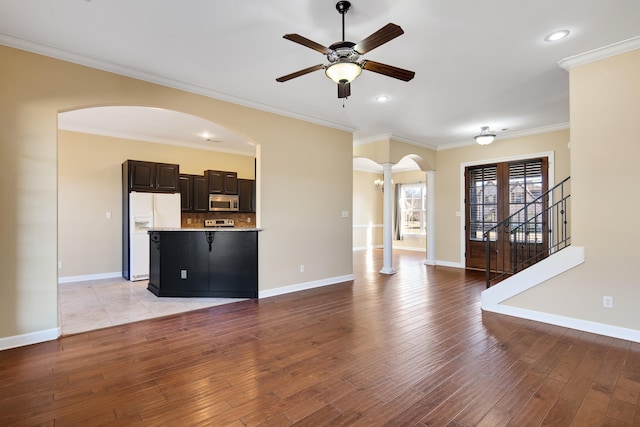 unfurnished living room with arched walkways, light wood finished floors, and crown molding