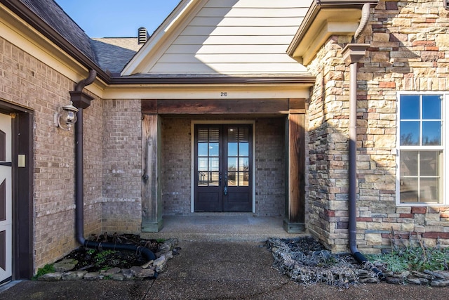 doorway to property with stone siding, french doors, roof with shingles, and brick siding