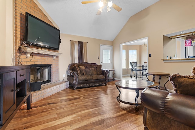 living room with lofted ceiling, ceiling fan, a fireplace, light hardwood / wood-style floors, and a textured ceiling