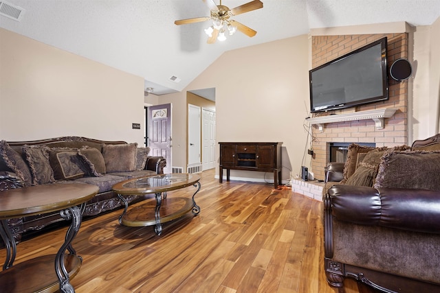 living room featuring lofted ceiling, ceiling fan, a fireplace, light hardwood / wood-style flooring, and a textured ceiling