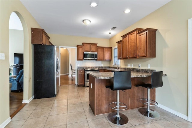 kitchen featuring appliances with stainless steel finishes, a kitchen bar, sink, kitchen peninsula, and light tile patterned floors