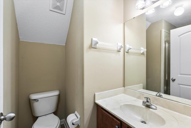 bathroom with a textured ceiling, toilet, lofted ceiling, and vanity