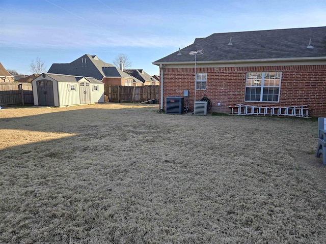 rear view of house with a lawn, central AC, and a storage unit