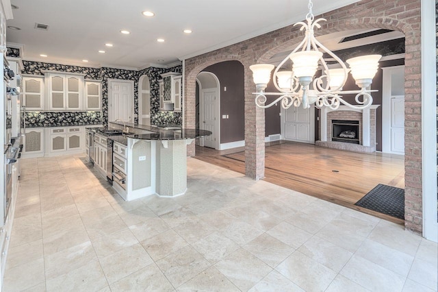 kitchen featuring backsplash, a fireplace, dark stone countertops, a center island, and an inviting chandelier