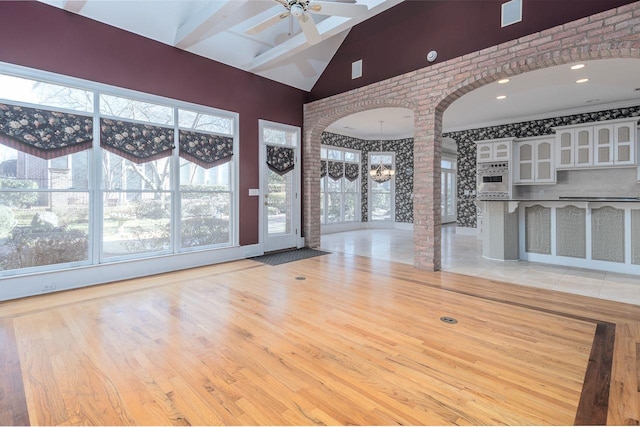 interior space featuring light wood-type flooring, a healthy amount of sunlight, ceiling fan with notable chandelier, and vaulted ceiling with beams