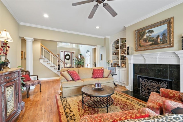 living room with built in features, ornamental molding, a tiled fireplace, and light hardwood / wood-style flooring