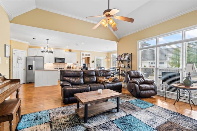 living room featuring ceiling fan with notable chandelier, light hardwood / wood-style floors, ornamental molding, and vaulted ceiling