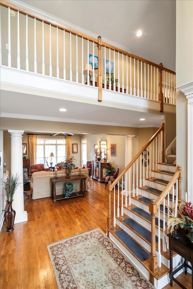 stairs featuring decorative columns, wood-type flooring, and ornamental molding