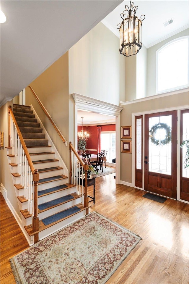 foyer entrance featuring ornamental molding, a towering ceiling, hardwood / wood-style flooring, and a notable chandelier