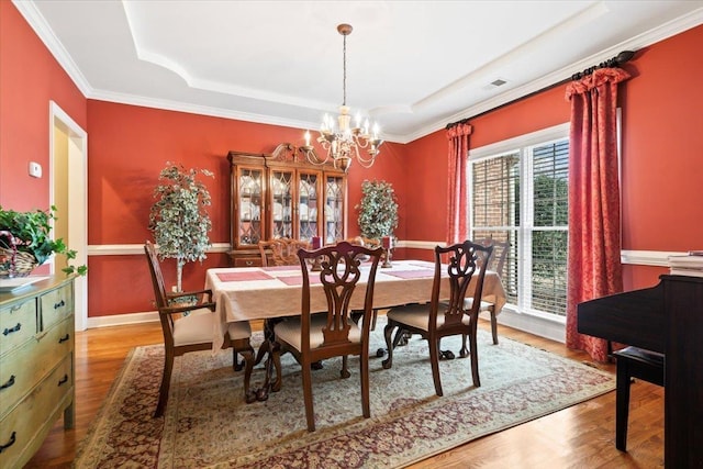 dining area featuring hardwood / wood-style floors, crown molding, a raised ceiling, and a notable chandelier