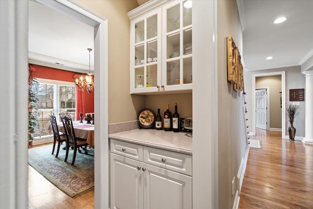 bar featuring white cabinetry, crown molding, a chandelier, and light wood-type flooring