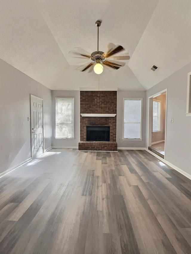 unfurnished living room with vaulted ceiling, a fireplace, plenty of natural light, and a textured ceiling