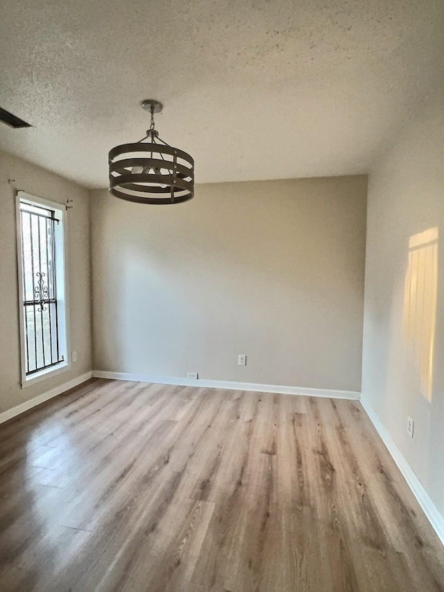 unfurnished dining area featuring a textured ceiling, hardwood / wood-style floors, and a notable chandelier