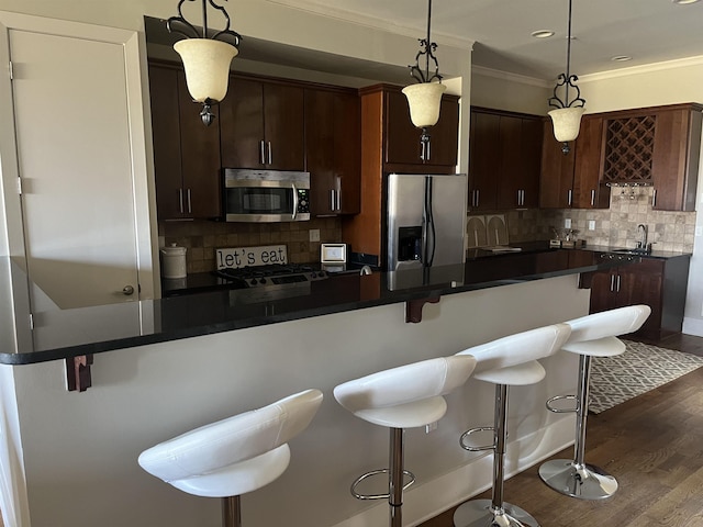 kitchen featuring hanging light fixtures, dark brown cabinetry, stainless steel appliances, and a breakfast bar area